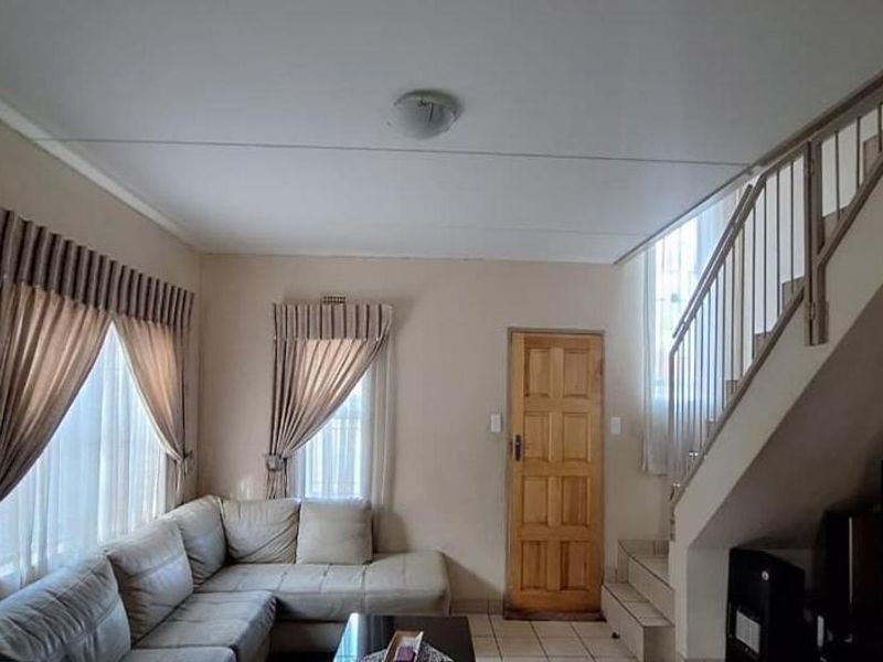 A living room featuring tiled flooring, a wooden entrance door, and an internal staircase with a metal balustrade.