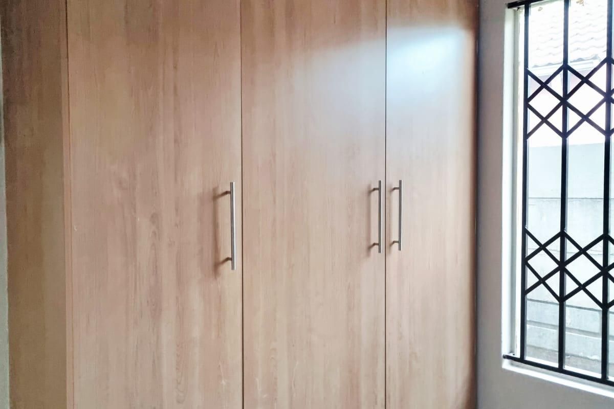 A bedroom featuring a large built-in wooden wardrobe, tiled flooring, and a window fitted with a security gate.