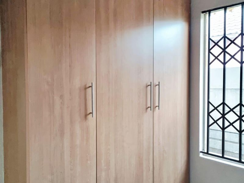 A bedroom featuring a large built-in wooden wardrobe, tiled flooring, and a window fitted with a security gate.