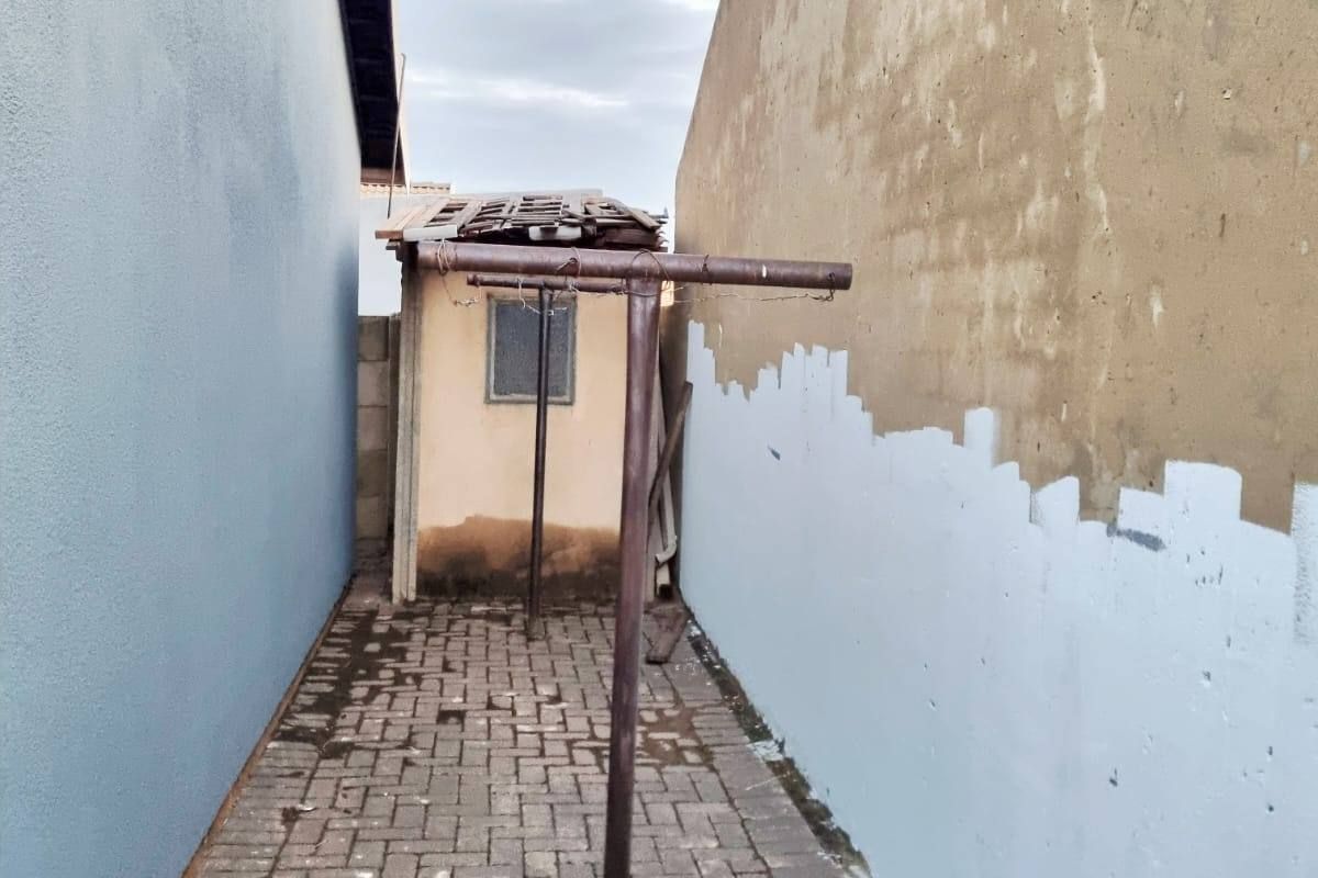 A narrow side passage featuring paved flooring, a metal washing line, and a small utility structure with a damaged roof.