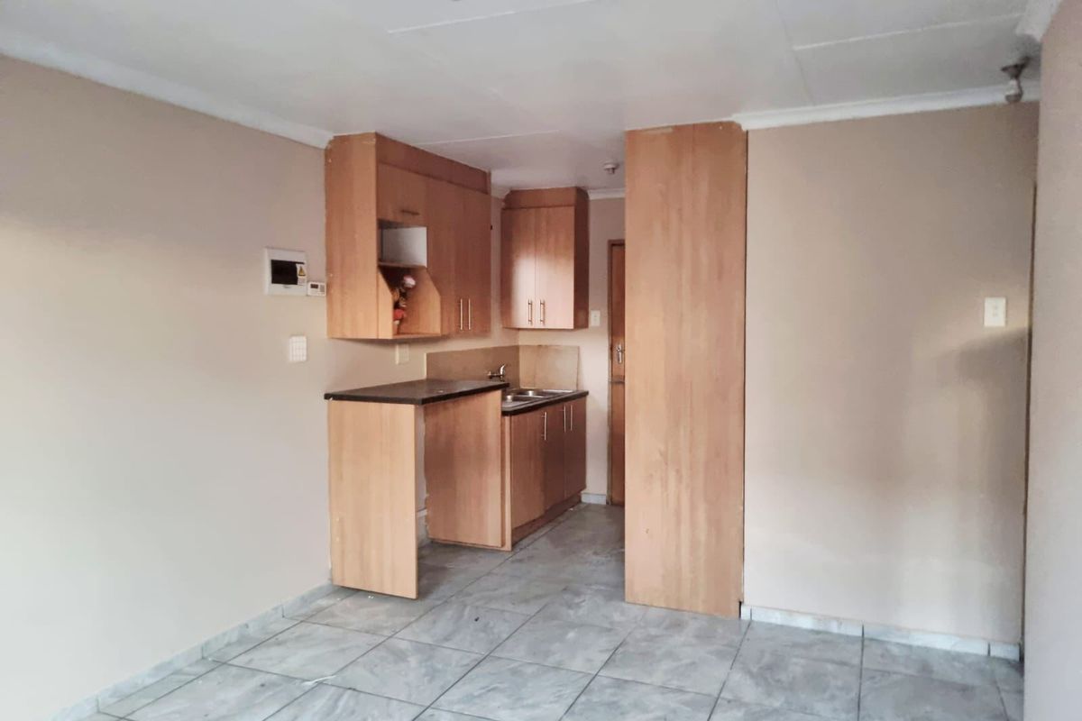 A compact kitchen area featuring laminate cabinetry, a stainless steel sink, and tiled flooring, presenting a functional space ready for modernization.