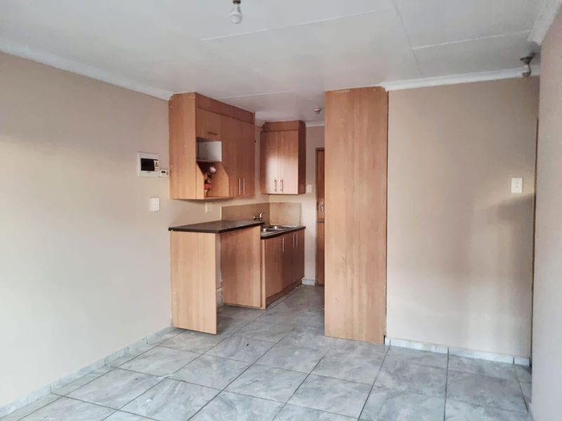 A compact kitchen area featuring laminate cabinetry, a stainless steel sink, and tiled flooring, presenting a functional space ready for modernization.