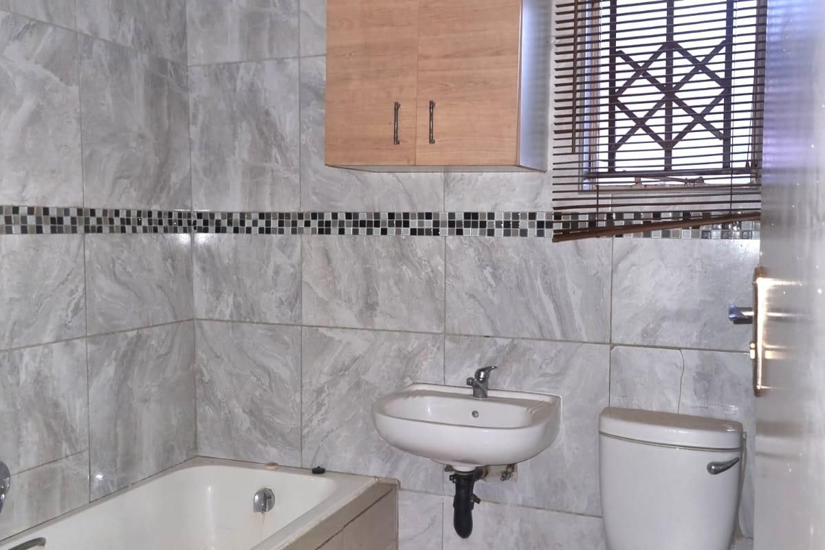 A functional bathroom featuring a bathtub, wall-mounted basin, toilet, and neutral wall tiling with a decorative mosaic border.
