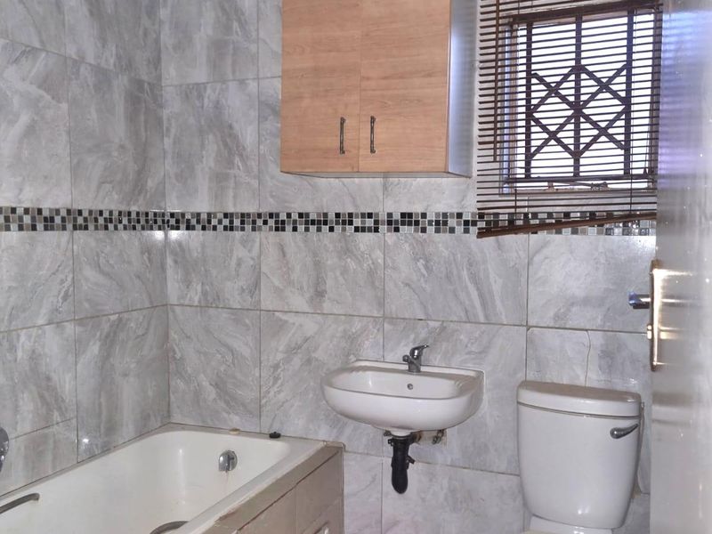 A functional bathroom featuring a bathtub, wall-mounted basin, toilet, and neutral wall tiling with a decorative mosaic border.