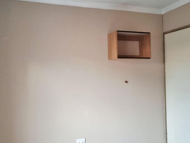 A simple, empty bedroom featuring neutral wall paint, tiled flooring, and a wall-mounted storage unit.