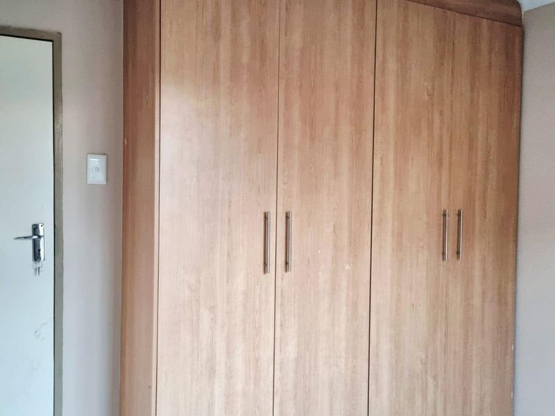 A bedroom featuring a large built-in wooden wardrobe, tiled flooring, and a standard internal door.