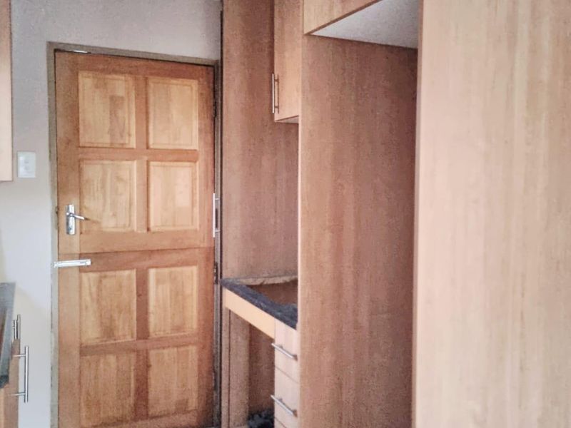 A functional kitchen area featuring built-in wooden cabinetry, tiled flooring, and a solid wood door, offering a blank canvas for potential updates.