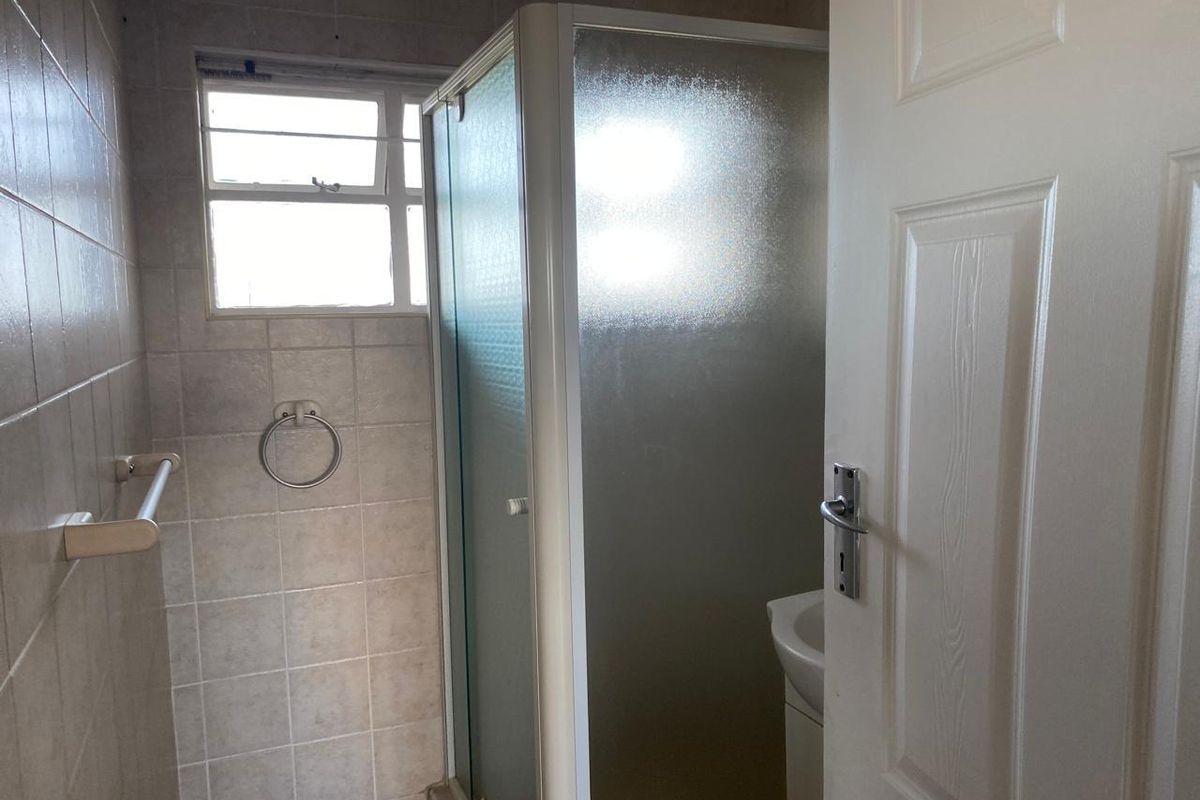 A functional bathroom featuring a shower enclosure, tiled walls, and a window, providing a clean and practical space.