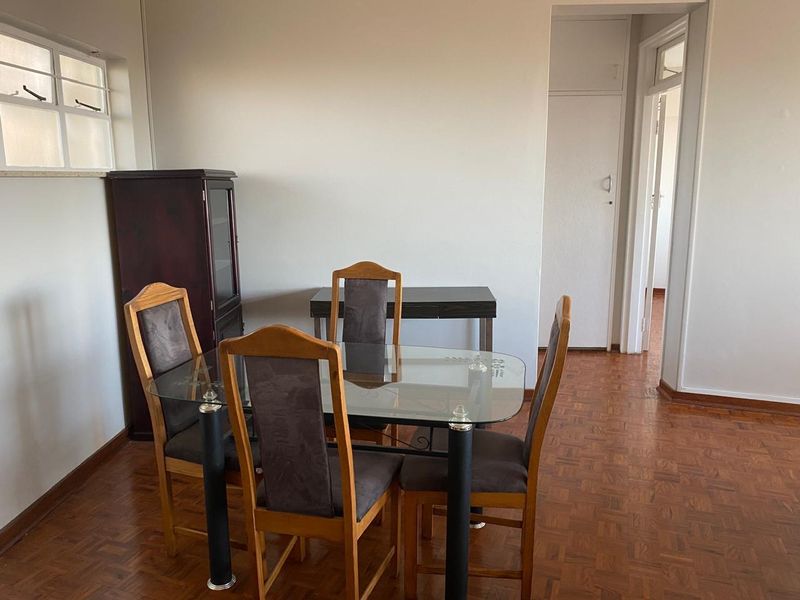 A dining area featuring classic parquet flooring and a side window, providing a functional space with access to an adjacent hallway.