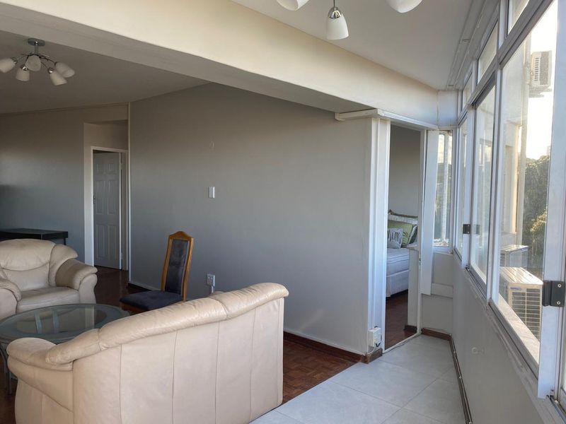 Spacious living area featuring a mix of parquet and tiled flooring, large windows providing natural light, and direct access to an adjacent bedroom.