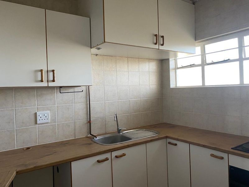 A functional kitchen featuring laminate countertops, built-in white cabinetry, a stainless steel sink, and tiled backsplash with natural light from the window.
