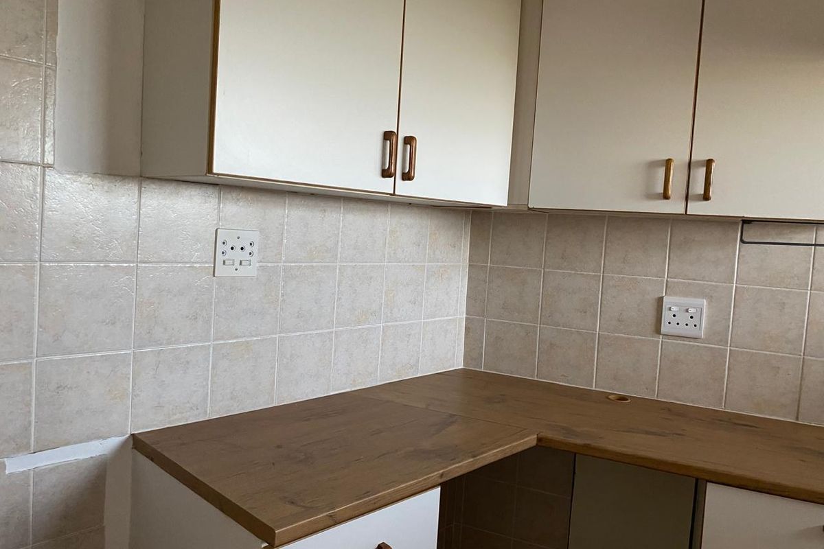 A dated kitchen corner featuring laminate countertops, wall-mounted and base cabinetry, and a ceramic tile backsplash, requiring minor finishing touches.