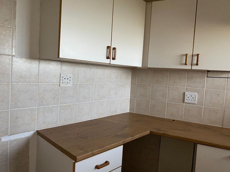 A dated kitchen corner featuring laminate countertops, wall-mounted and base cabinetry, and a ceramic tile backsplash, requiring minor finishing touches.