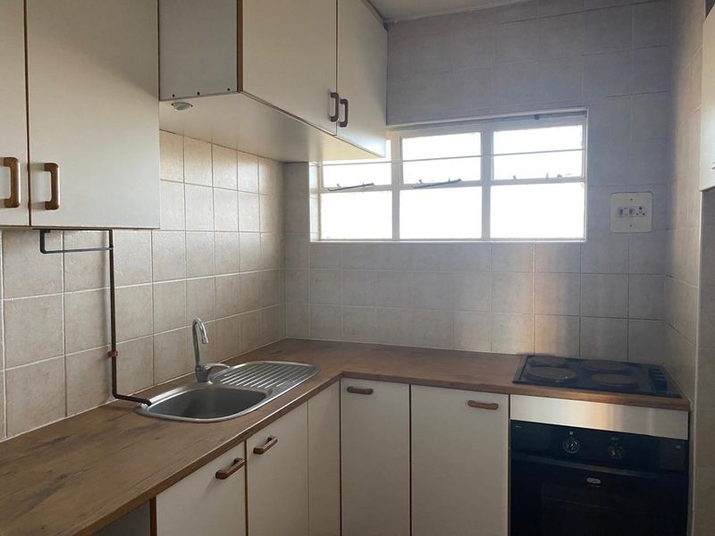 A functional kitchen featuring built-in cabinetry, a laminate countertop, stainless steel sink, and integrated electric oven and hob with tiled splashbacks.