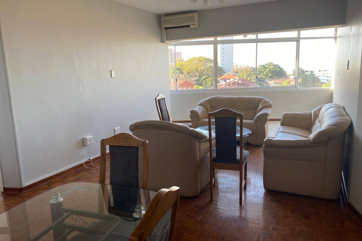 Spacious living area featuring parquet flooring, large sliding windows providing natural light, and a wall-mounted air conditioning unit.