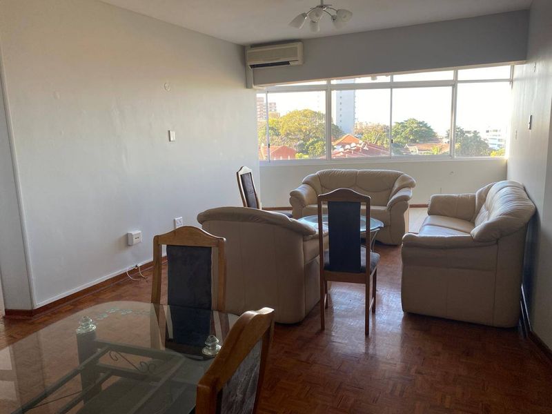 Spacious living area featuring parquet flooring, large sliding windows providing natural light, and a wall-mounted air conditioning unit.