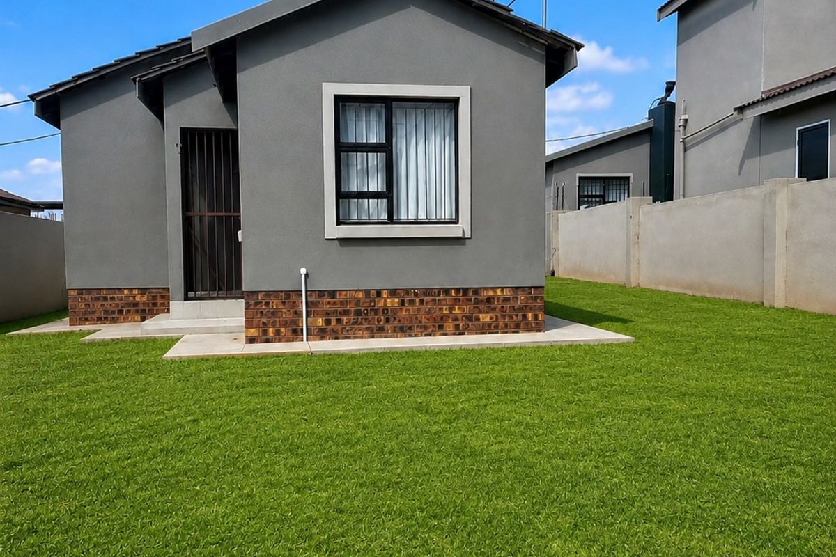 A well-maintained rear exterior view of a modern house featuring a neat lawn, brick plinth detailing, and secure aluminium window frames.