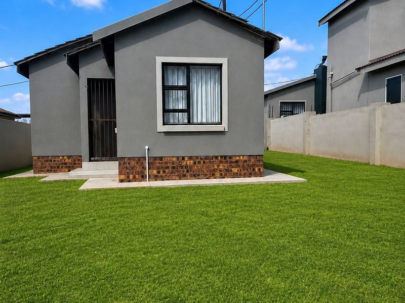 A well-maintained rear exterior view of a modern house featuring a neat lawn, brick plinth detailing, and secure aluminium window frames.