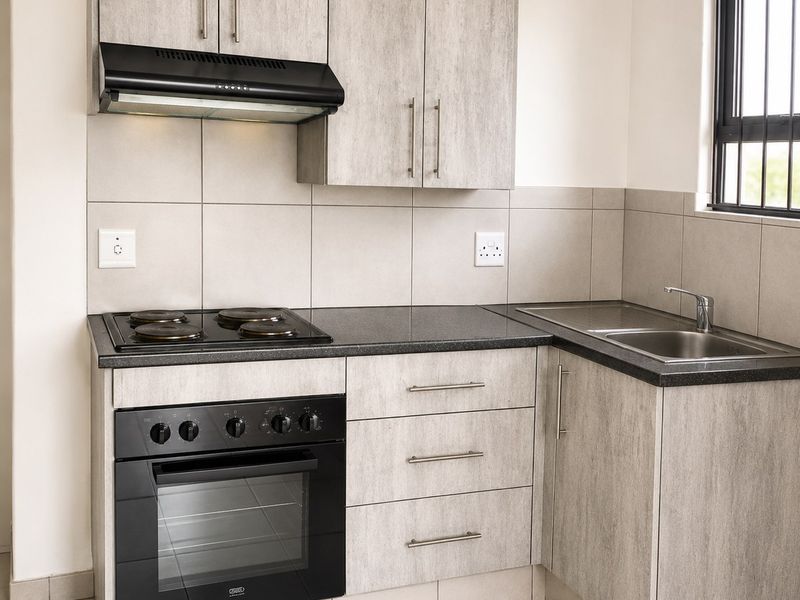 Modern kitchen featuring light wood-grain cabinetry, dark countertops, built-in oven and hob, extractor fan, and stainless steel sink with tiled finishes.