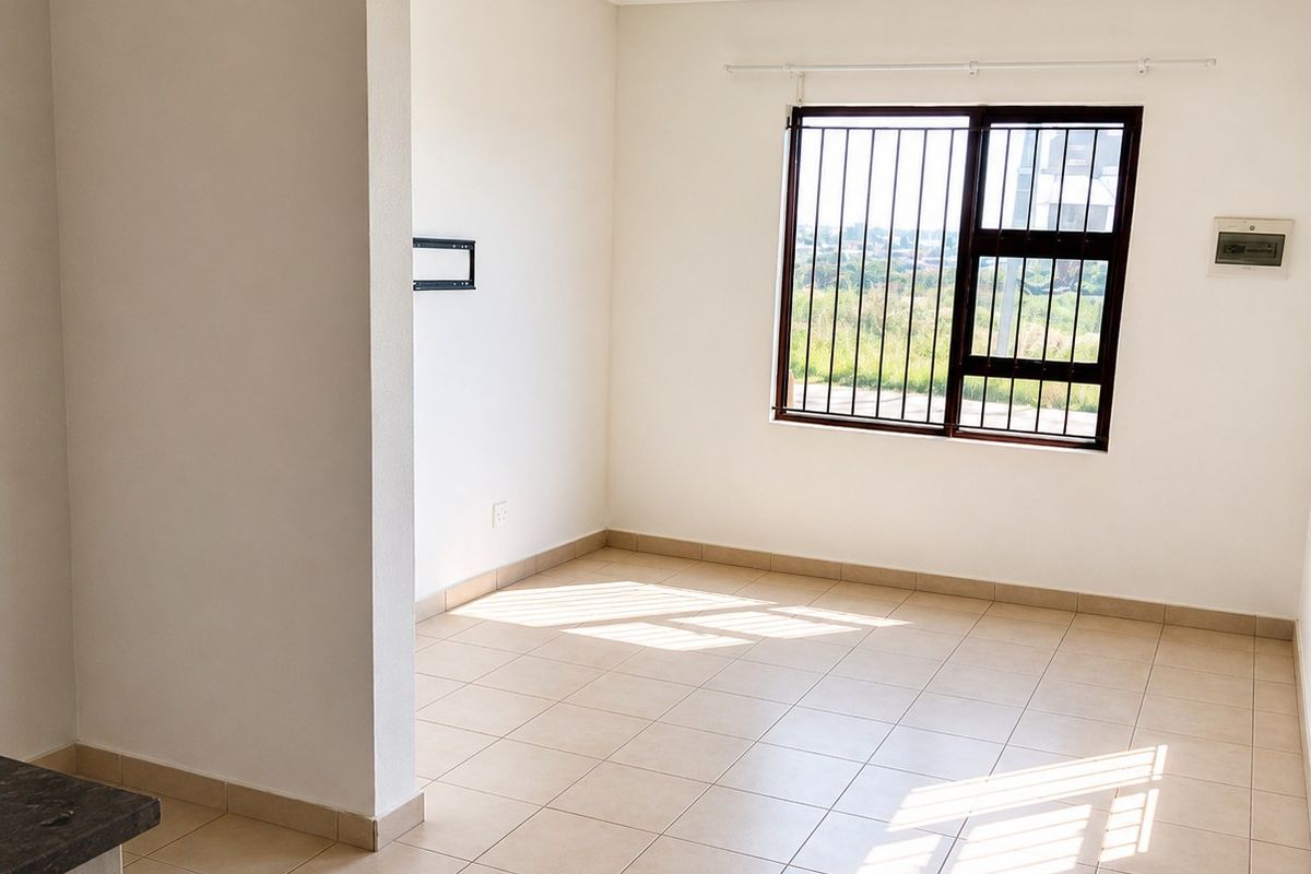 A bright, empty living area featuring neutral tiled flooring, clean white walls, and a window fitted with security bars.