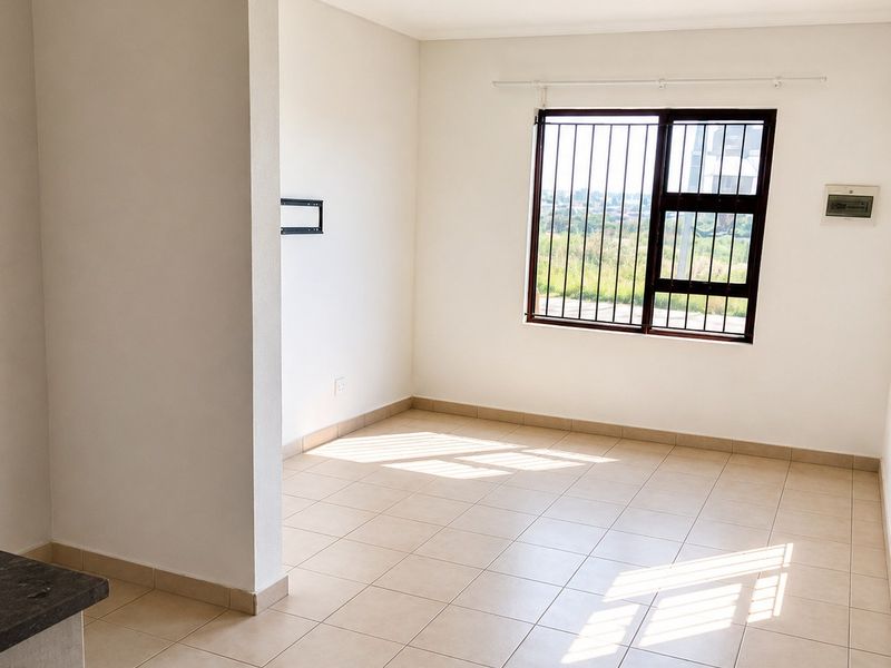 A bright, empty living area featuring neutral tiled flooring, clean white walls, and a window fitted with security bars.