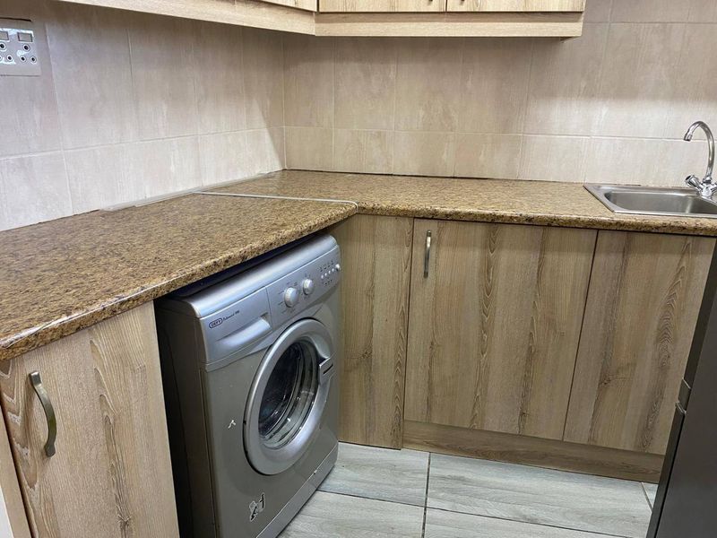 A functional kitchen area featuring wood-look laminate cabinetry, granite countertops, a stainless steel sink, and a built-in washing machine.
