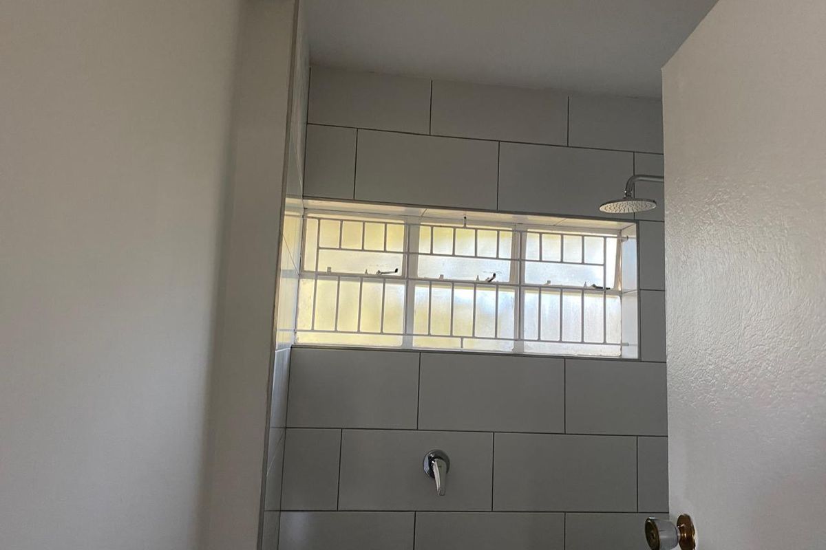 A clean, tiled shower area featuring a modern shower head, mixer, and a frosted window with security bars for privacy and safety.