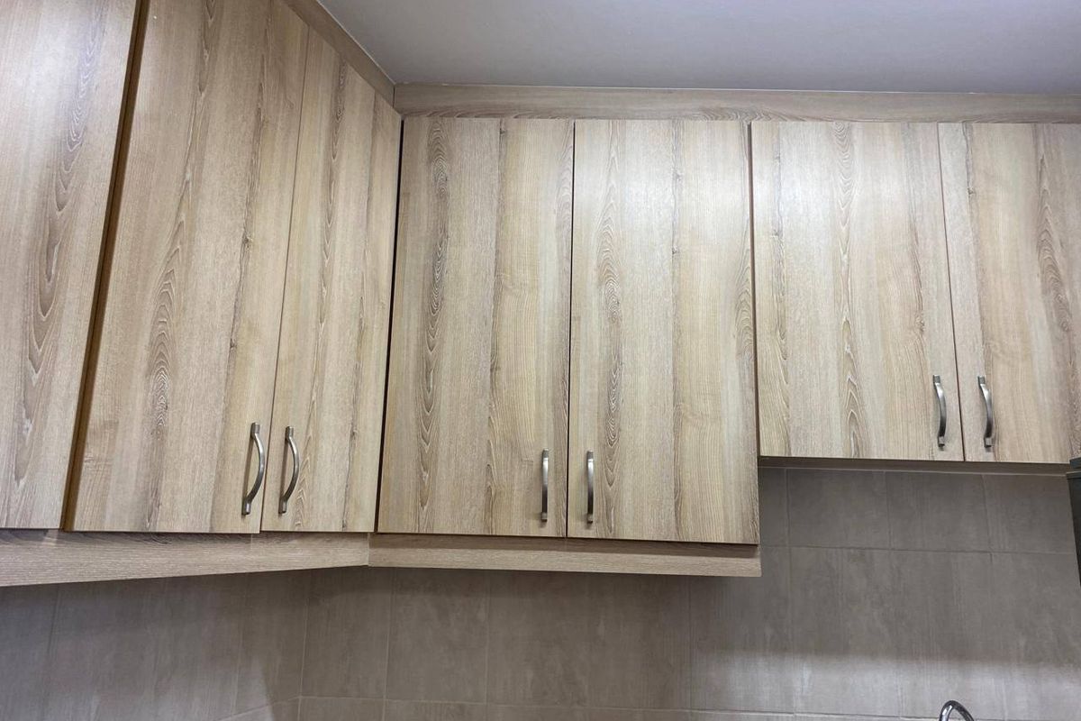 A close-up view of kitchen cabinetry featuring light wood-grain laminate doors and a neutral tiled backsplash.