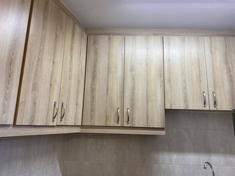 A close-up view of kitchen cabinetry featuring light wood-grain laminate doors and a neutral tiled backsplash.