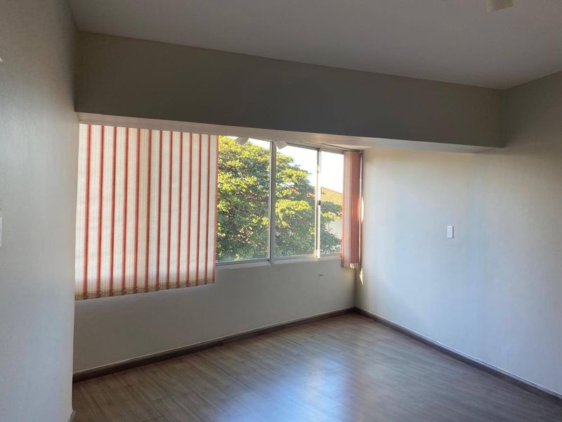 An empty bedroom featuring laminate flooring, vertical blinds, and a large sliding window providing natural light and a view of the surrounding trees.