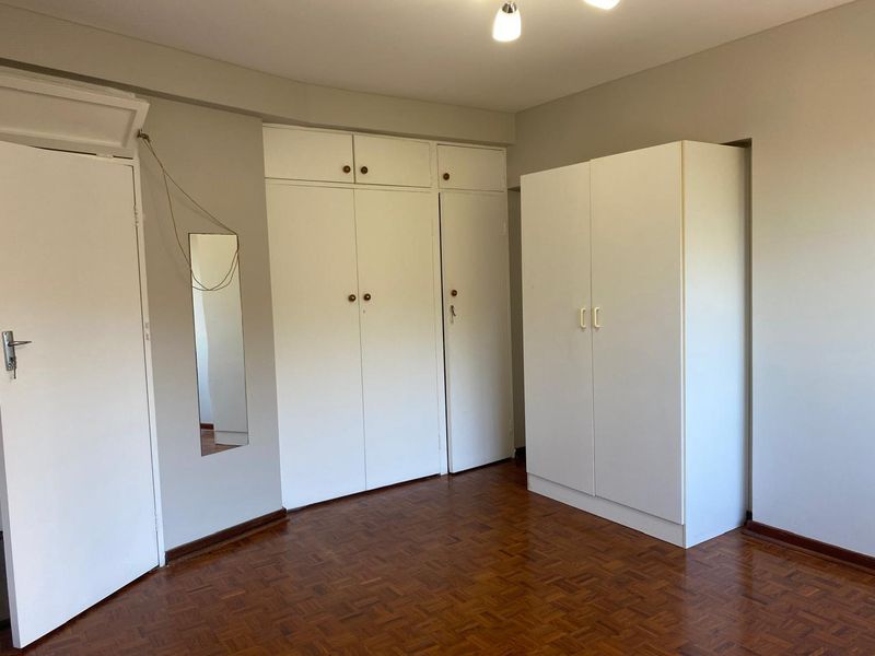 A bedroom featuring classic parquet flooring and ample built-in cupboard storage, offering a neutral canvas for potential interior updates.