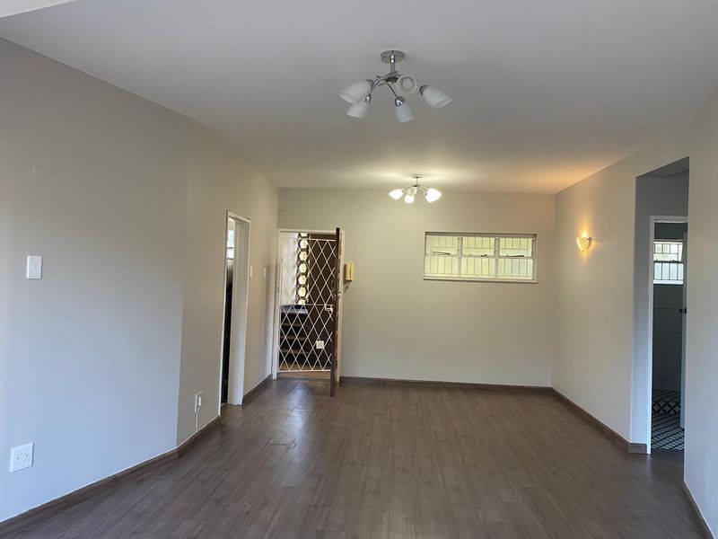 A spacious, empty living area featuring laminate flooring, neutral walls, and multiple lighting fixtures, including a security gate at the entrance.