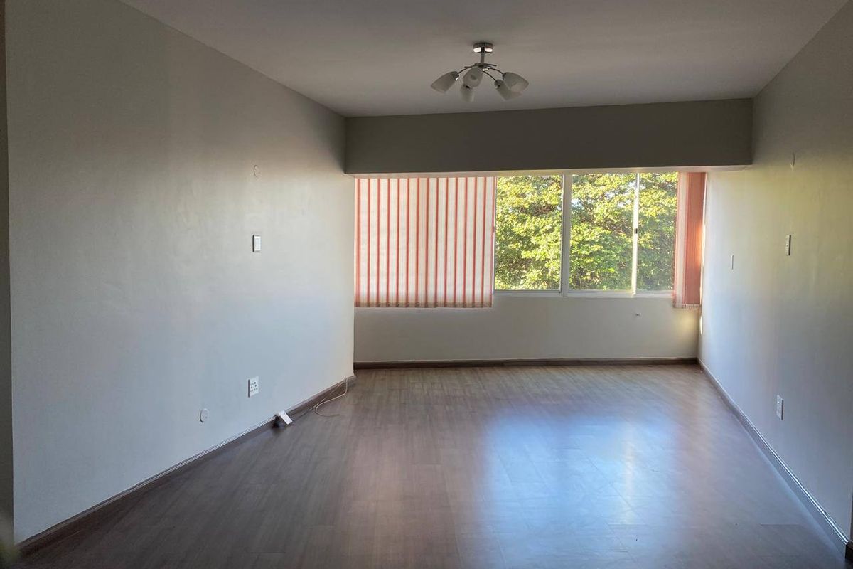 A spacious, empty living room featuring laminate flooring, neutral walls, and large windows with vertical blinds, offering a blank canvas for interior design.