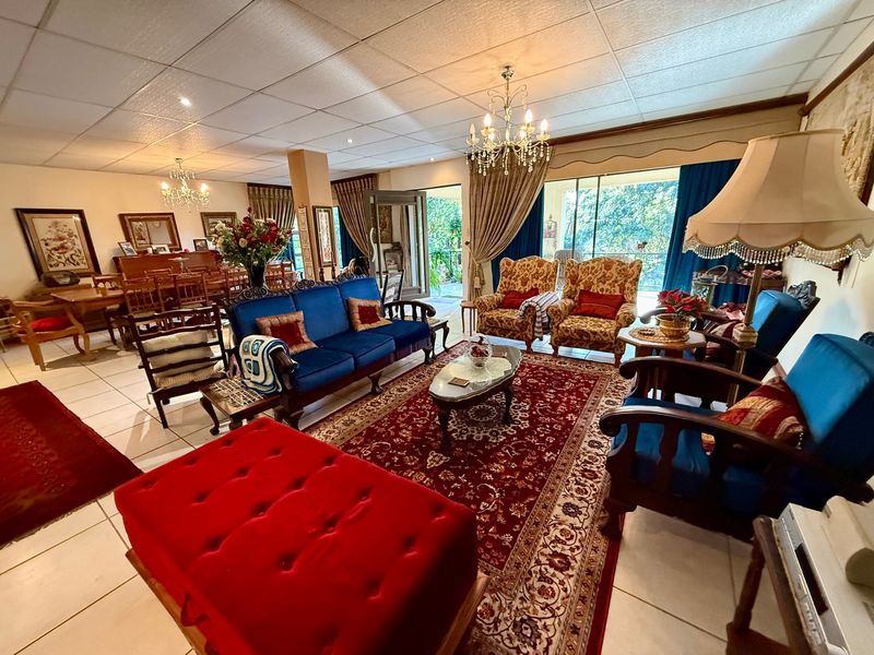 Spacious open-plan living and dining area featuring tiled flooring, drop ceilings, elegant chandeliers, and large sliding glass doors leading to the outdoor space.