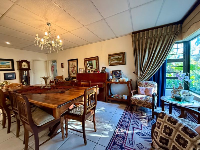 A spacious dining room featuring tiled flooring, a classic chandelier, and a large bay window that allows for ample natural light.