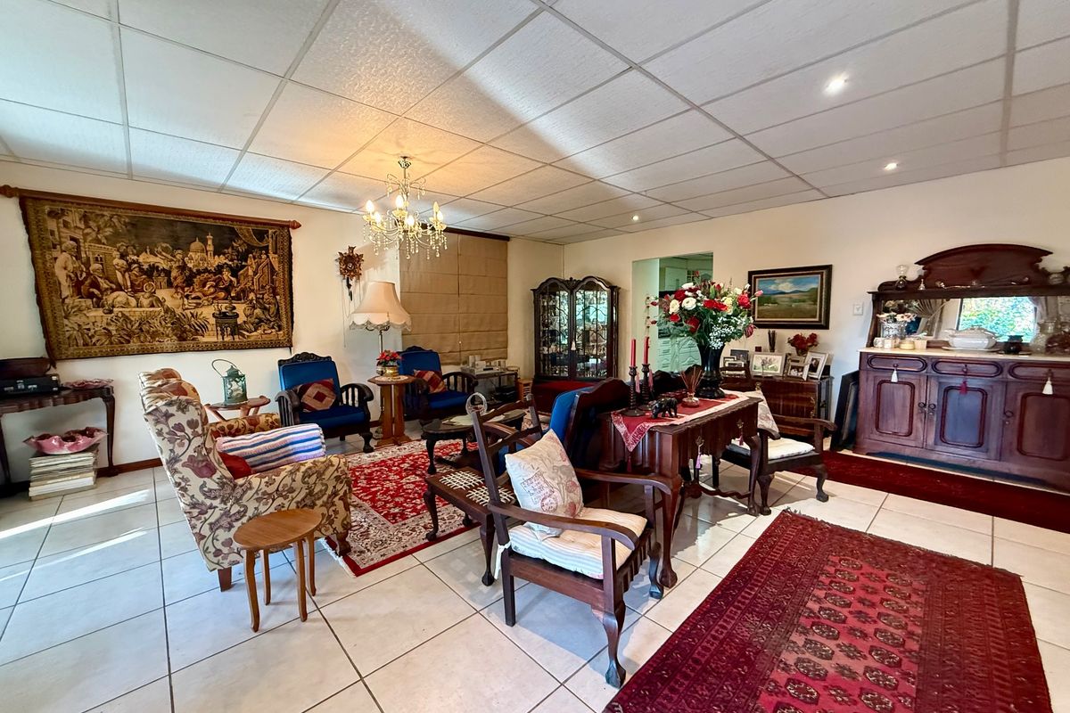 Spacious living room featuring tiled flooring, a suspended ceiling with recessed lighting, and a central chandelier, offering a versatile layout for comfortable seating arrangements.