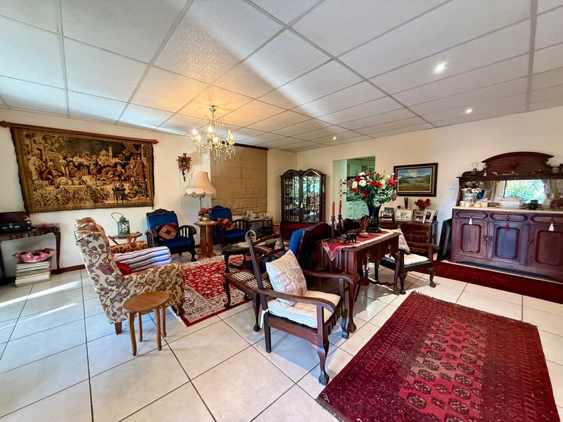 Spacious living room featuring tiled flooring, a suspended ceiling with recessed lighting, and a central chandelier, offering a versatile layout for comfortable seating arrangements.