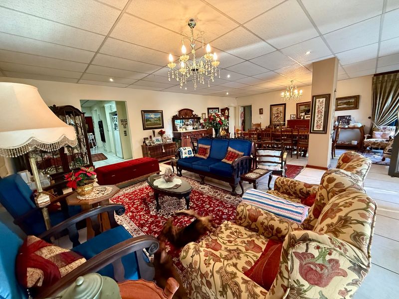 Spacious open-plan living and dining area featuring tiled flooring, decorative crystal chandeliers, and a suspended ceiling design.
