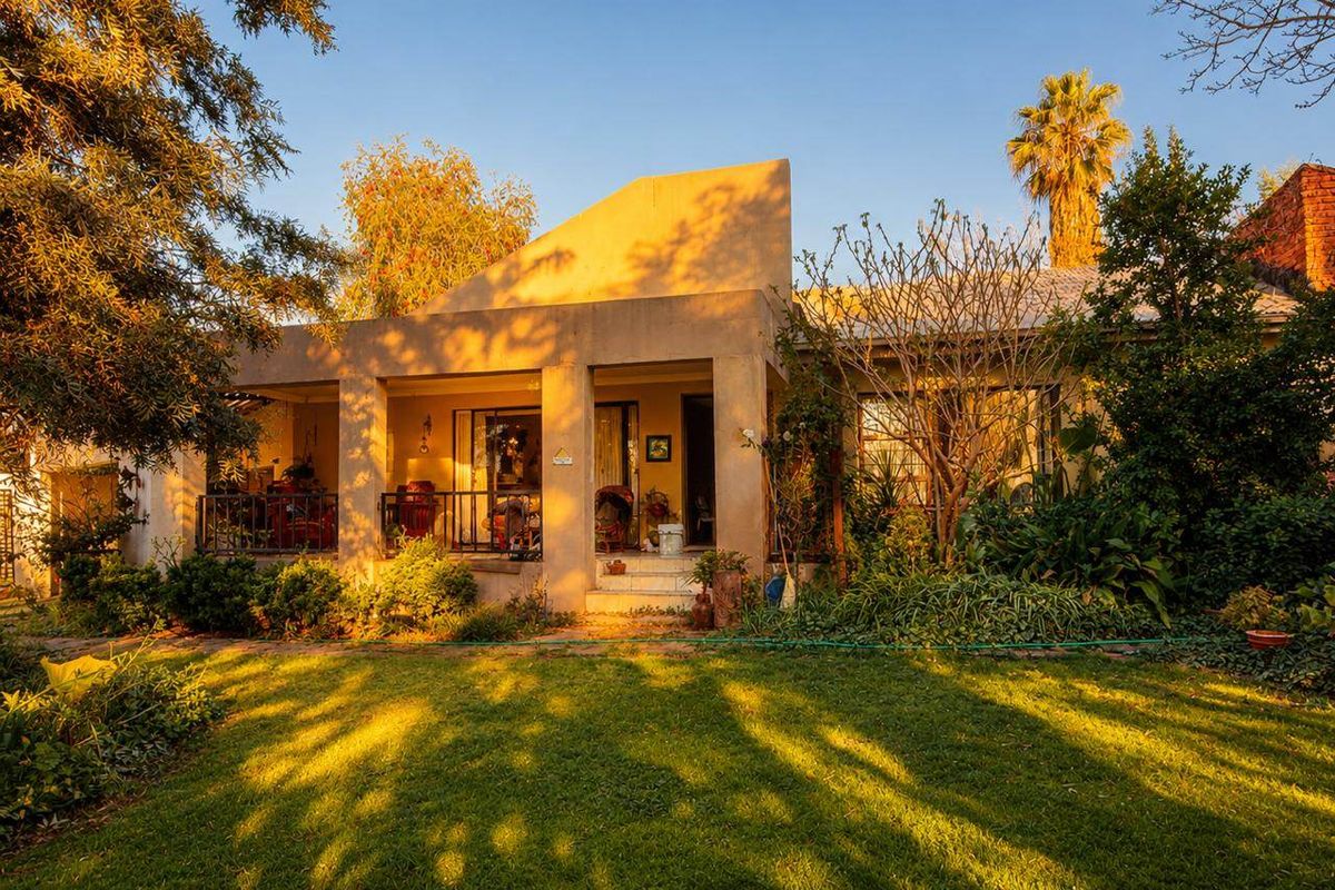 A rear view of the house featuring a covered patio with concrete pillars, metal railings, and a well-maintained garden area.