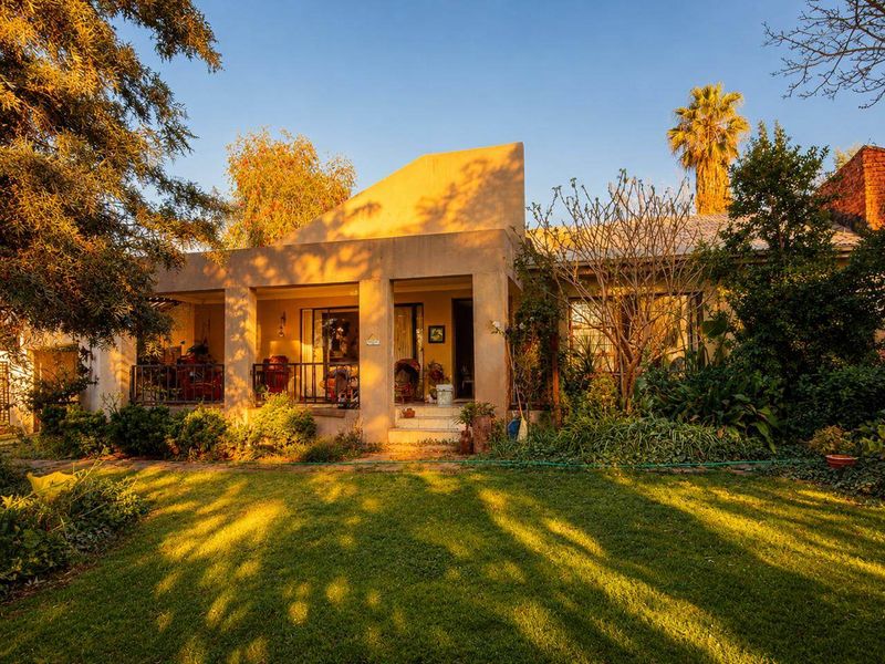 A rear view of the house featuring a covered patio with concrete pillars, metal railings, and a well-maintained garden area.