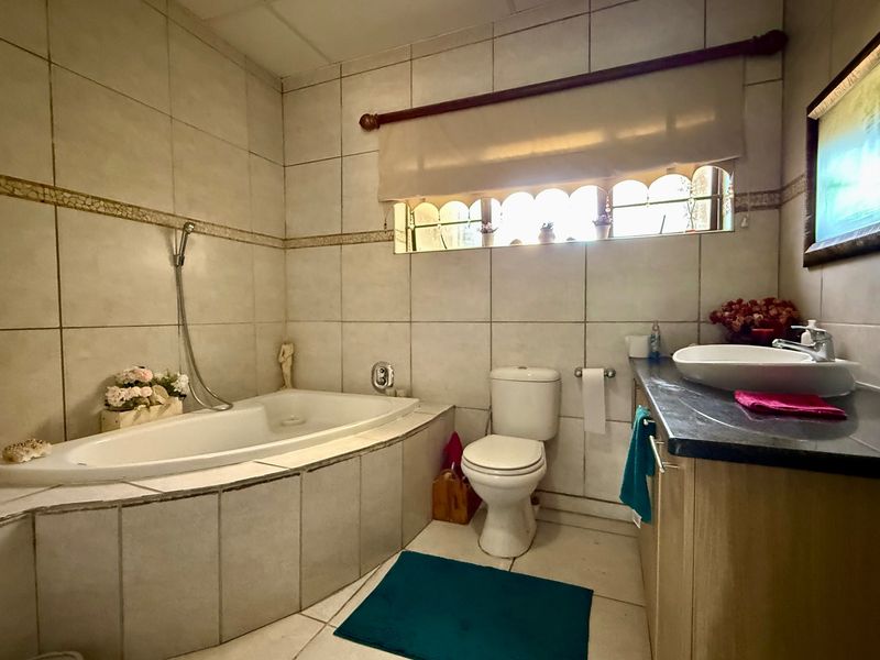 A functional bathroom featuring a built-in bathtub, a vessel sink vanity, and neutral wall tiling throughout.