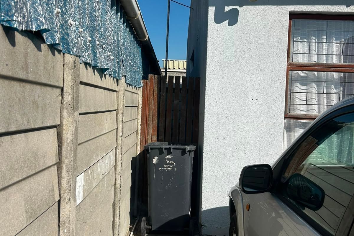 A narrow side passage featuring a precast concrete boundary wall, paved flooring, and exterior building access with guttering and antenna infrastructure.