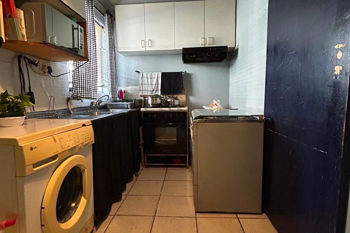 Compact kitchen featuring built-in cabinetry, tiled flooring, and integrated appliances, currently showing signs of wear and ceiling water damage.