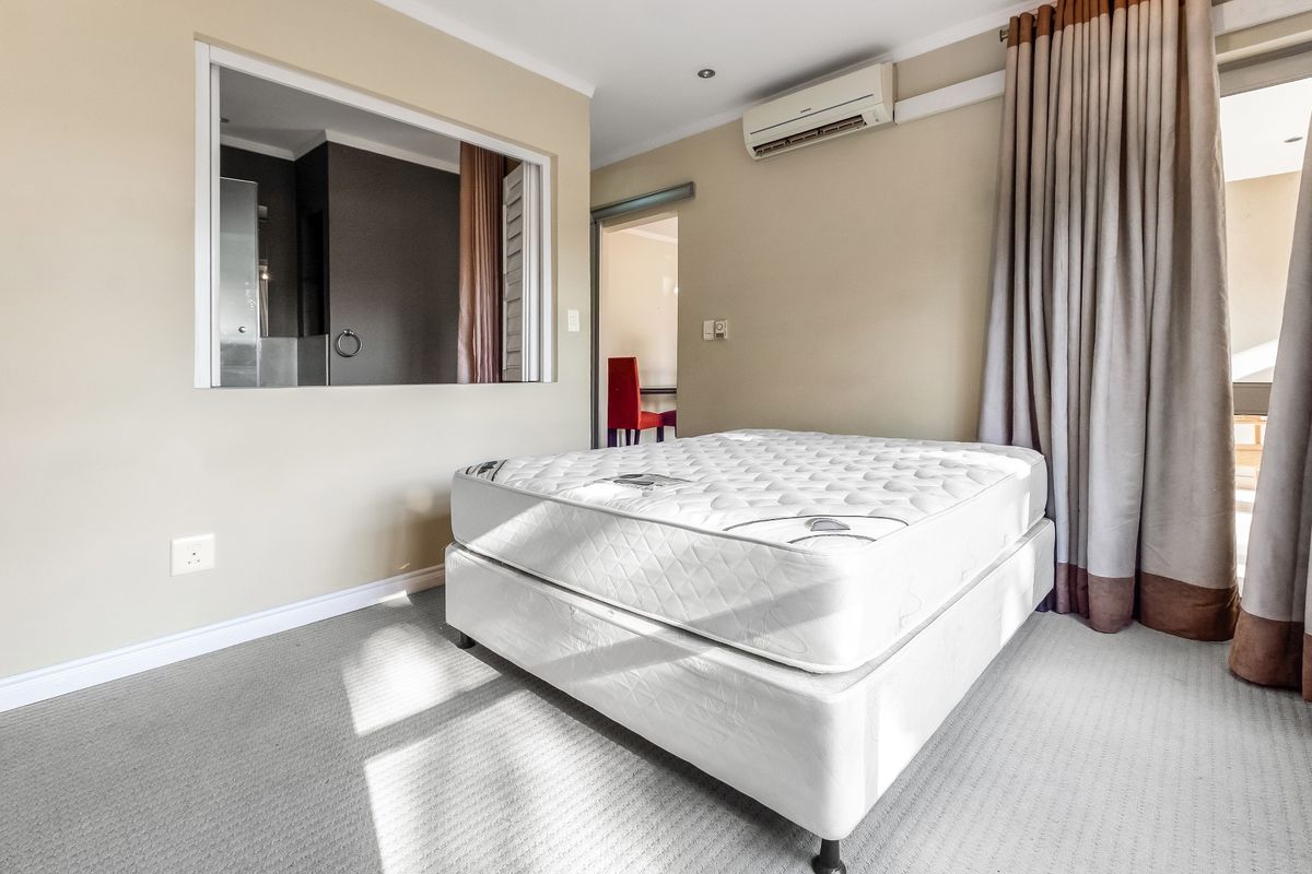 Spacious bedroom featuring neutral walls, carpeted flooring, an integrated air conditioning unit, and an internal window looking into the bathroom area.