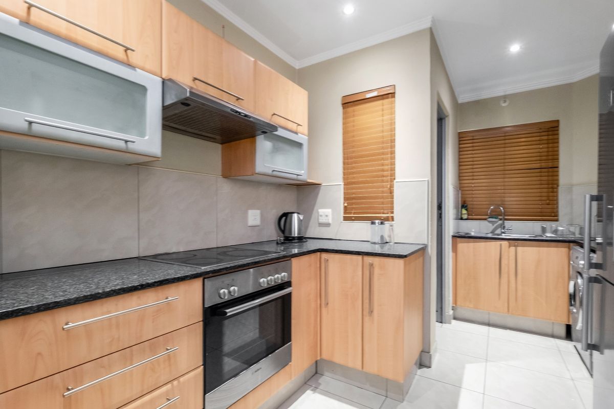 A functional kitchen featuring light wood cabinetry, granite countertops, built-in oven and hob, and a separate scullery area with a sink.