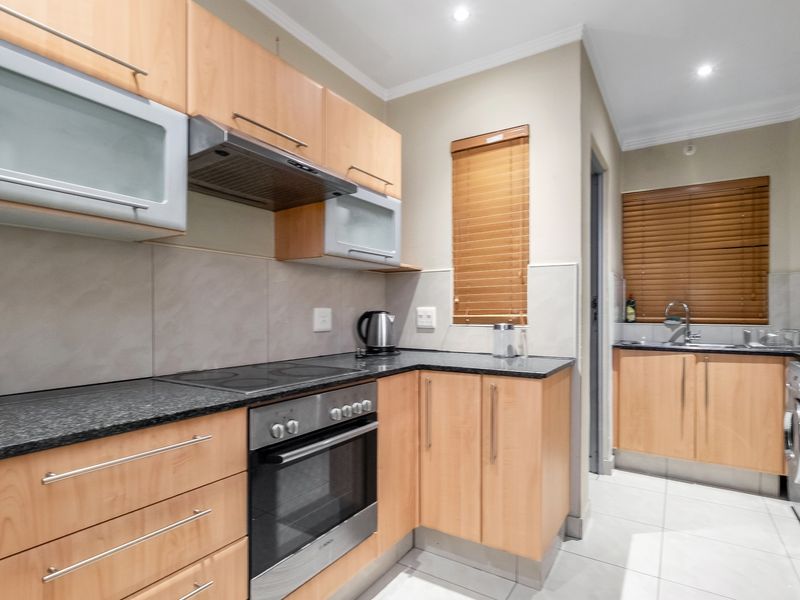 A functional kitchen featuring light wood cabinetry, granite countertops, built-in oven and hob, and a separate scullery area with a sink.