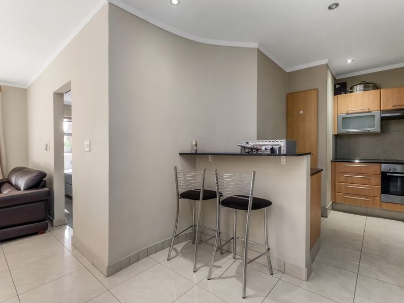 Open-plan kitchen and living area featuring modern cabinetry, integrated appliances, a breakfast bar, and neutral tiled flooring throughout.