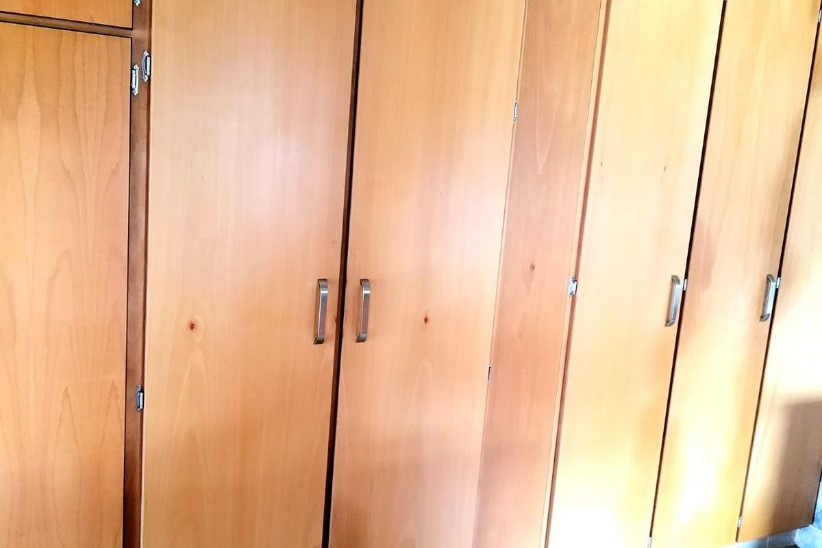 A bedroom interior featuring extensive built-in wooden cabinetry with metal handles, providing ample storage space.
