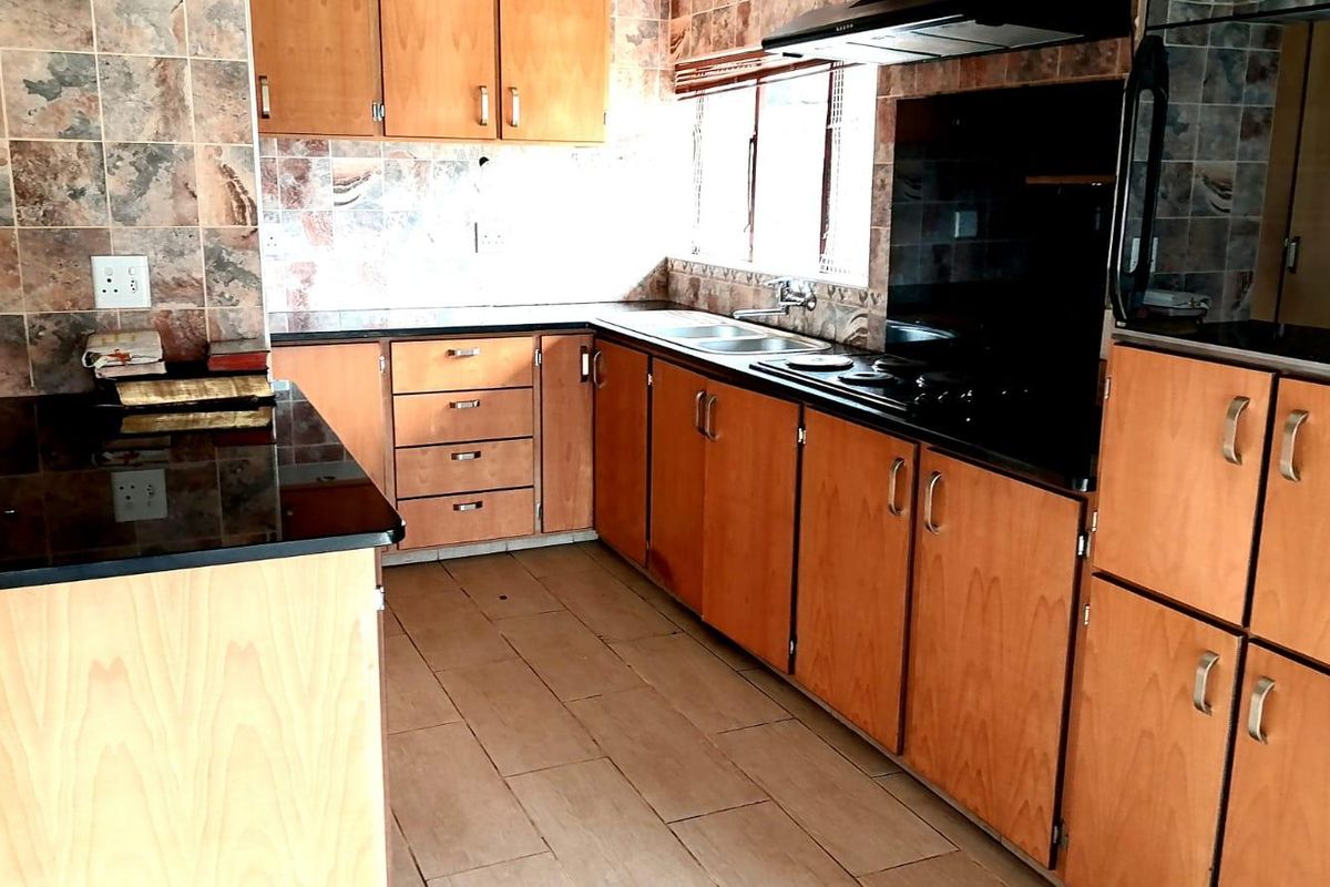 A functional kitchen featuring laminate cabinetry, granite countertops, a built-in hob with extractor fan, and tiled finishes throughout.