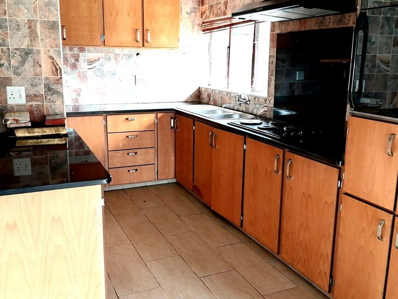 A functional kitchen featuring laminate cabinetry, granite countertops, a built-in hob with extractor fan, and tiled finishes throughout.